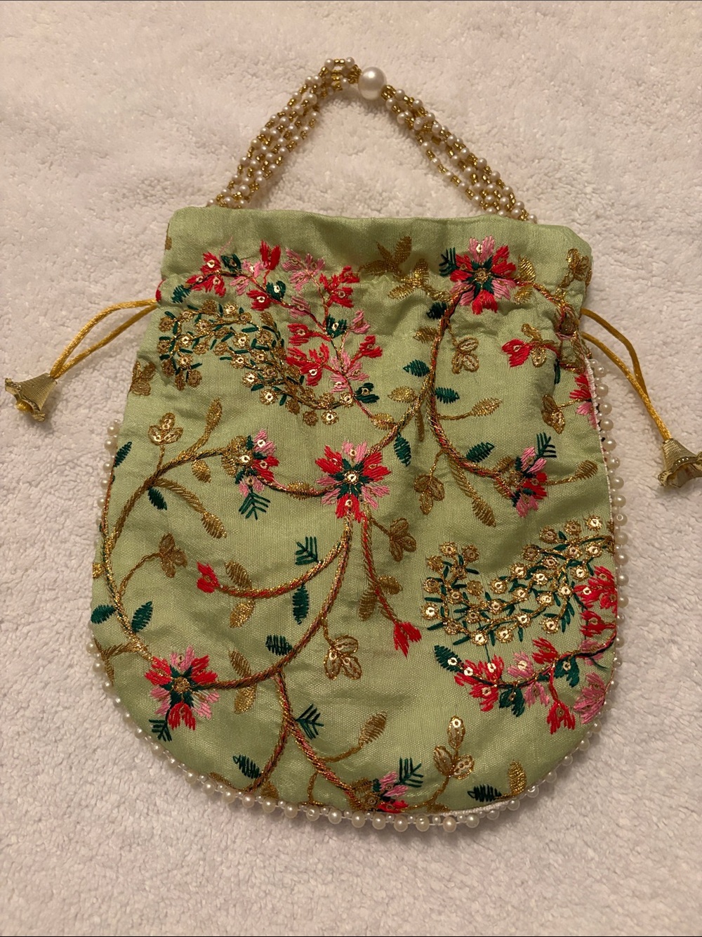 Embroidered potli bag with pearl handle and bell tassels.
